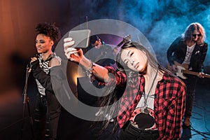 Young woman taking selfie with rock and roll band performing concert