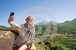 Young woman taking selfie or vlogging on mobile phone during her travel on the island