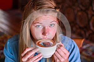 Young woman taking a sip of coffee with her face printed on.