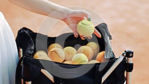 young woman taking tennis balls out of a bag on a court