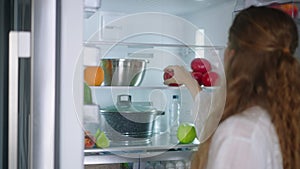 Young woman taking vegetables from fridge. Girl getting a tomato from refrigerator. Female having something healthy for