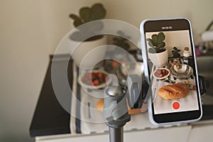 A young woman taking a video with her smartphone while making breakfast