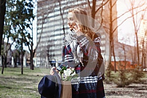 Young woman talking with boyfriend on cell telephone walking on a sunny day in the park. Beautiful girl in a coat, hat