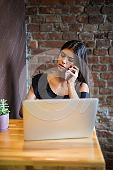 Young woman talking on cell phone and using laptop in cafe