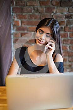 Young woman talking on cell phone and using laptop in cafe