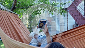 A young woman talking with friend on phone by video calling while lying in a hammock