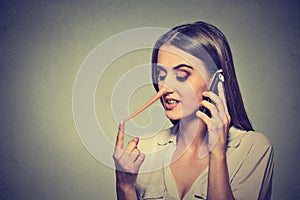 Young woman talking on mobile phone telling lies has a long nose