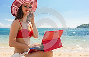 Young woman talking on mobile phone while using a tablet on the beach