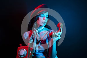 Young Woman Talking on Orange Retro Phone. High Fashion model woman in colorful bright neon blue and purple lights posing in
