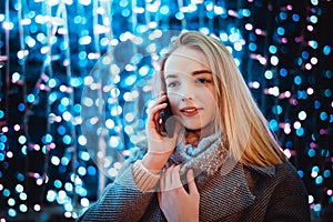 Young woman talking on the phone against the background of festive lights