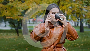 Young woman talking on phone with her boyfriend agrees meet cheerful beautiful girl resting on weekend in park drinking