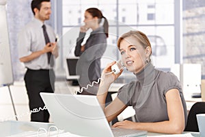 Young woman talking on phone in office smiling