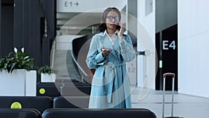 Young woman talking on phone and smiling while walking through airport interior.