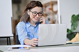 Young woman talking on the phone using laptop working online.