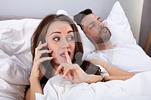 Woman talking privately on phone while husband sleeping on bed photo