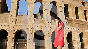 Young woman talking by smartphone in front of colosseum in Rome, Italy. Girl enjpy her italian vacation