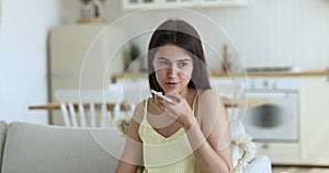 Young woman talking on speakerphone sit on couch at home