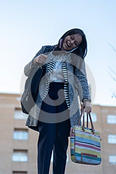 Young woman talking to phone holding between her ear and shoulder while carrying her bags in both hands