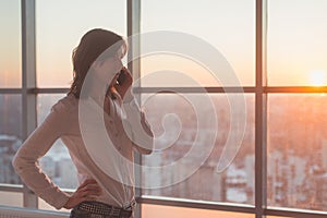 Young woman talking using cell phone at office in the evening. Female businesswoman concentrated, looking forward