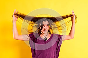 Young woman tangling her hair with her hands in disgust with her physical appearance, isolated on yellow background