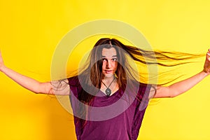 Young woman tangling her hair with her hands in disgust with her physical appearance,  on yellow background