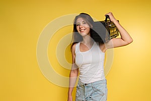 Young woman in a tank top and denim shorts with a retro tape recorder on a yellow background. The photo