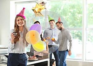 Young woman with tasty muffin and air balloons at birthday party in office