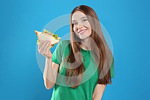 Young woman with tasty sandwich on blue background