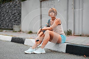 Young woman with tattoo is sitting on the sidewalk with a cup of coffee in her hands. Waiting alone girl. The concept of