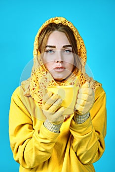 Young woman with tea mug in her hands. model in yellow clothes. blue background. autumn concept