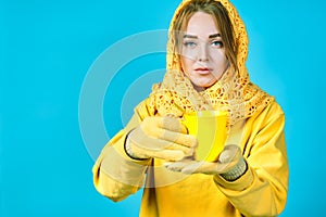 Young woman with tea mug in her hands. model in yellow clothes. blue background. autumn concept. copy space
