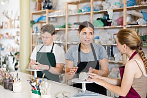 Young woman teacher helps teenagers boy and girl to sculpt ceramic product