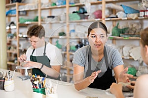 Young woman teacher helps teenagers boy and girl to sculpt ceramic product