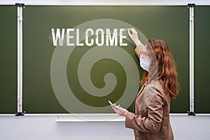 Young woman teacher with a phone in hand writes the text welcome back to school. Concept of problems at school during the