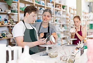 Young woman teaches teenage boy and teenage girl to paint ceramic cup