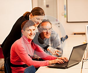 Young woman teaching elderly couple of computer skills. Intergenerational transfer of knowledge.