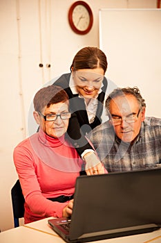 Young woman teaching elderly couple of computer skills. Intergenerational transfer of knowledge.