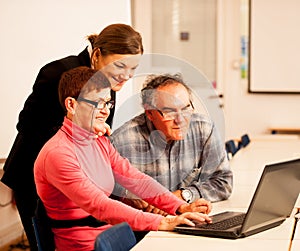 Young woman teaching elderly couple of computer skills. Intergenerational transfer of knowledge.