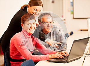 Young woman teaching elderly couple of computer skills. Intergenerational transfer of knowledge.