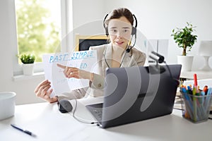 Young woman is teaching english with laptop computer, camcorder and headphone online at home. Teacher is having video conference