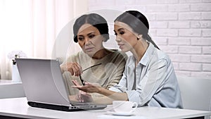 Young woman teaching grandma to use computer app, writing email, generation gap