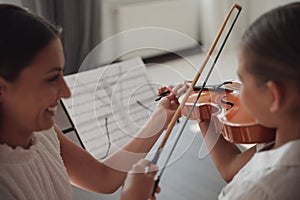 Young woman teaching little girl to play violin indoors, focus on hands