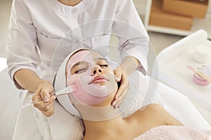 Young woman or teen girl enjoying cosmetic clay facial mask in spa and beauty salon