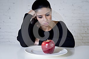 Young woman or teen looking apple fruit on dish as symbol of crazy diet in nutrition disorder