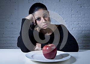 Young woman or teen looking apple fruit on dish as symbol of crazy diet in nutrition disorder