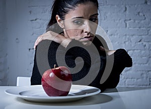 Young woman or teen looking apple fruit on dish as symbol of crazy diet in nutrition disorder