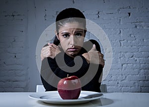 Young woman or teen looking apple fruit on dish as symbol of crazy diet in nutrition disorder