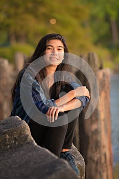 Young woman or teen sitting along lake pier at sunset