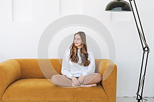 Young woman teenager in white hoodie beautiful girl sitting on yellow couch in the modern interior