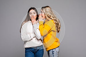 Young woman telling gossip to her girlfriend isolated over gray background